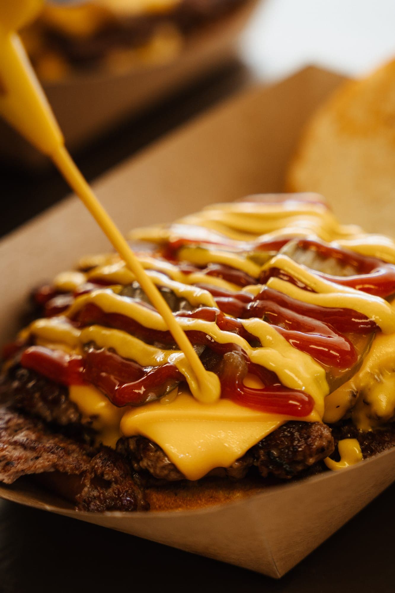 Smash burger papírtálcán, mustárral és ketchuppal meglocsolva, mellette a pirított felső buci